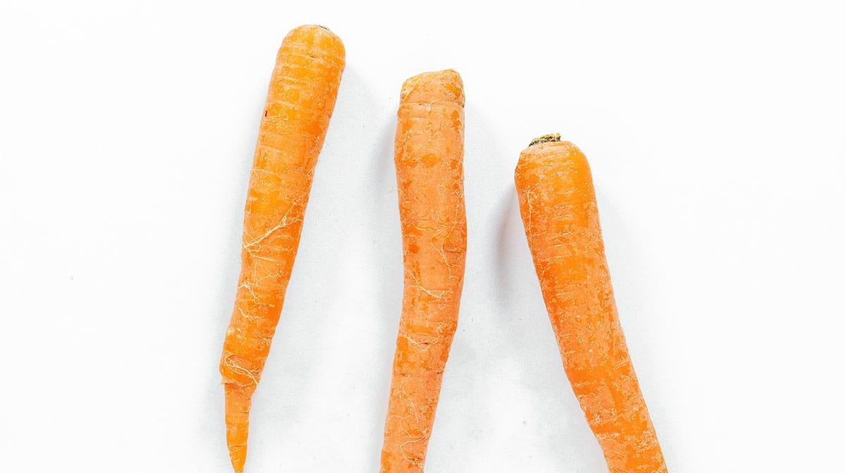 Ofengebackene Karotten-Chips 4 Drei Karotten auf weißem Hintergrund.