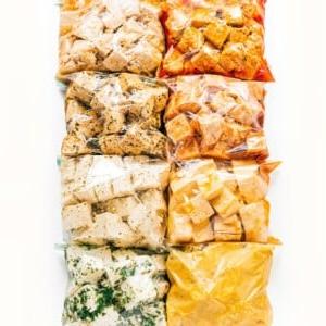 Wie man Tofu mariniert (8 Geschmacksrichtungen!) 32 Acht vakuumierte Beutel gefüllt mit verschiedenen Tofu-Würfeln, jeder mit einzigartigen Tofu-Marinaden, sind in zwei vertikalen Spalten auf einem weißen Hintergrund angeordnet.