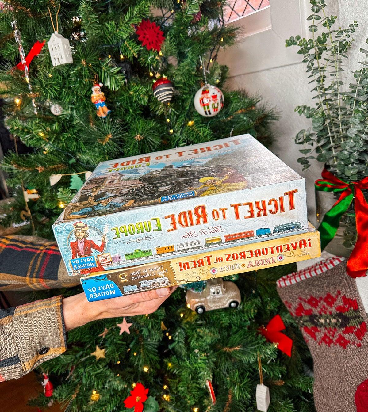 Brettspiele wie Ticket To Ride und Telestrations als Geschenk vor einem Weihnachtsbaum.