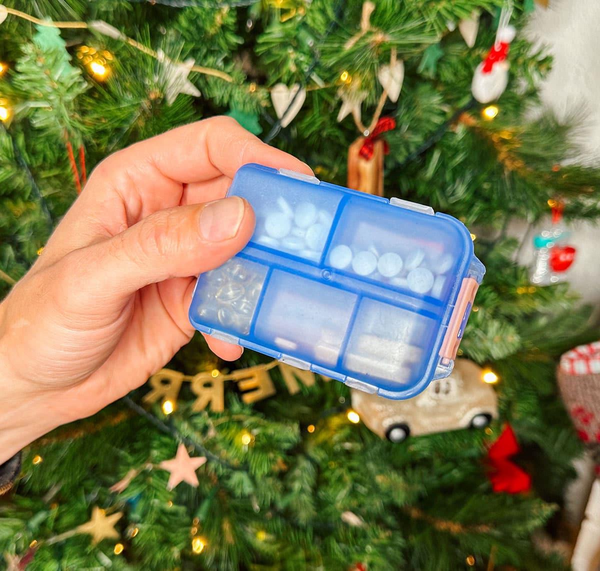 Eine kleine Reise-Pillendose als Geschenk vor einem Weihnachtsbaum.