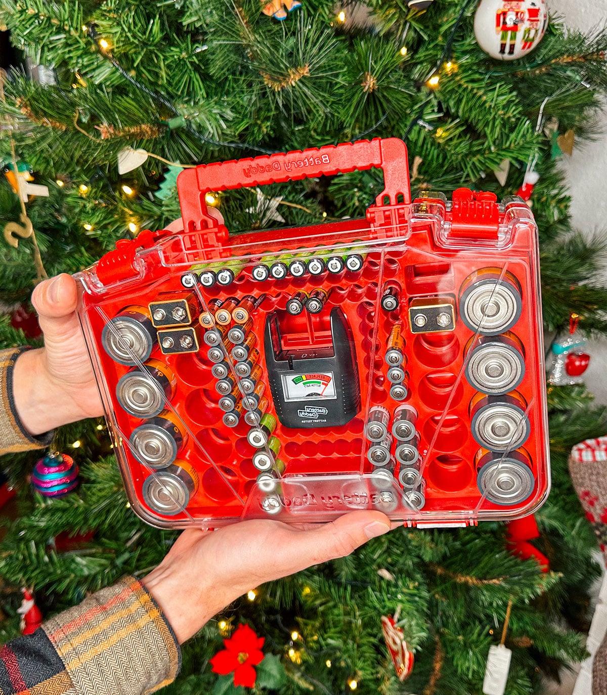 Ein Battery Daddy Batterie-Organizer als Geschenk vor einem Weihnachtsbaum.