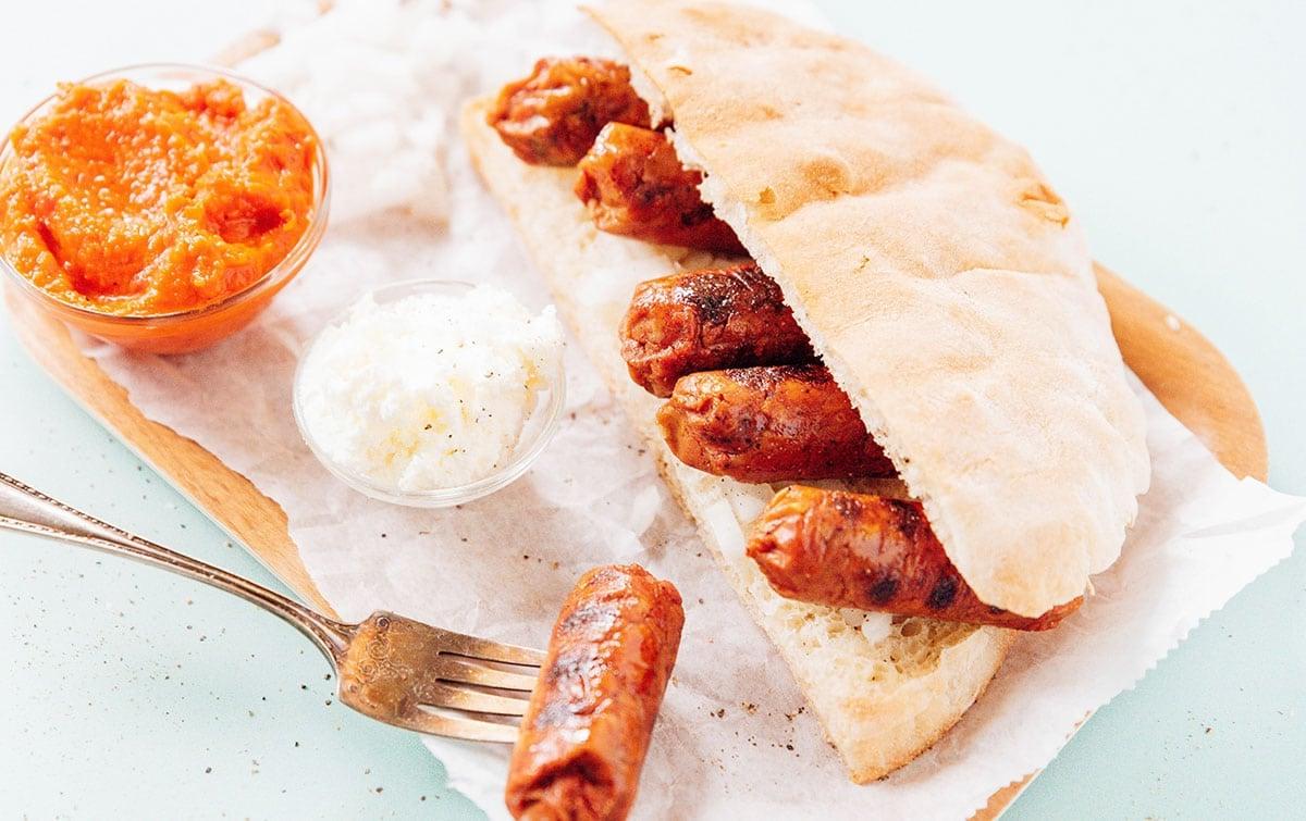 Vegetarische Cevapcici (Kroatisches Cevapi-Sandwich-Rezept) 5 Vegetarische Cevapi auf einem Teller mit Ajvar und Kajmak.