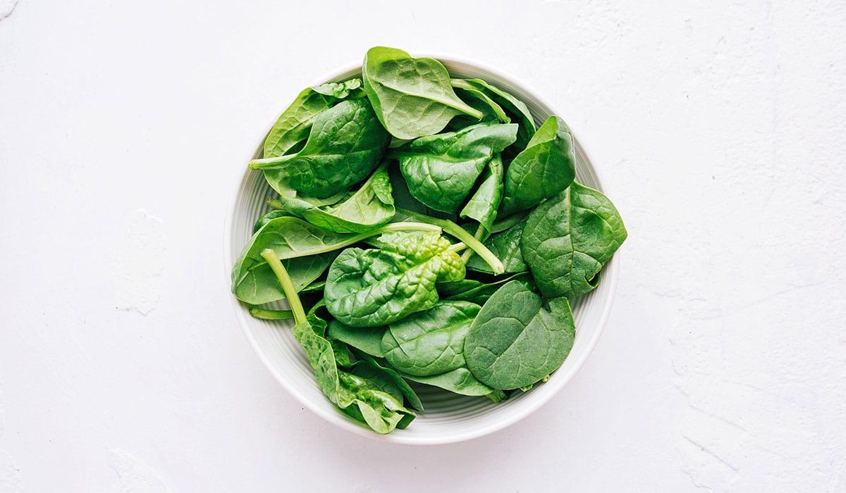 **Wie man eine Buddha Bowl zusammenstellt** 5 Spinat in einer Schüssel auf weißem Hintergrund