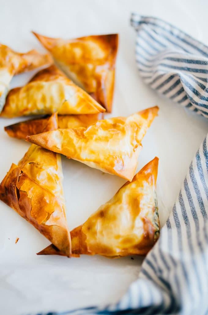 Spanakopita-Dreiecke (Kleine griechische Spinattörtchen!) 5 Nahaufnahme von perfekt gebackenen Spanakopita Dreiecken, einige sind aufgeschnitten und zeigen die reiche Spinat-Feta-Füllung und den knusprigen Filoteig.