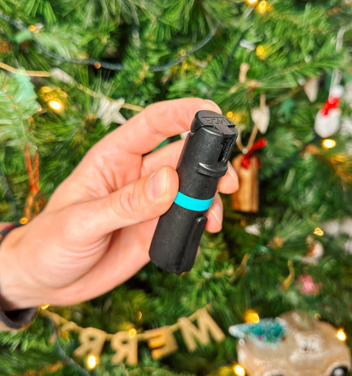 Pfefferspray als praktisches Geschenk vor einem Weihnachtsbaum.