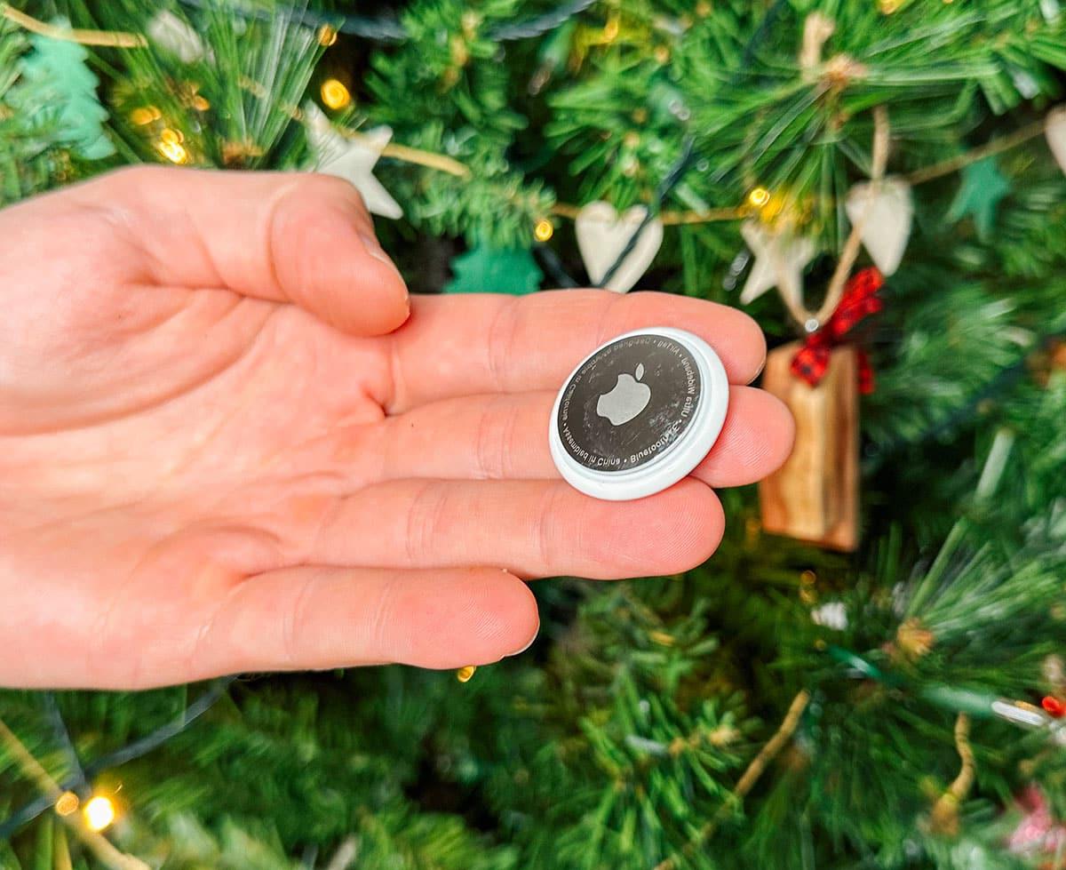 Ein Apple AirTag als Geschenk vor einem Weihnachtsbaum.