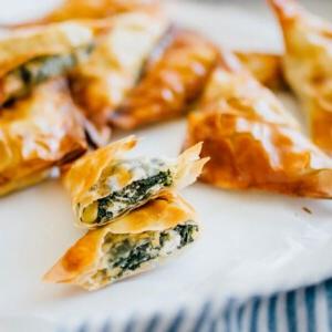 Spanakopita-Dreiecke (Kleine griechische Spinattörtchen!) 6 Wie man Spanakopita zubereitet, ein aufgeschnittenes Spanakopita Dreieck auf einem weißen Teller mit blauem Handtuch – Diese Spanakopita Dreiecke sind eine einfache Vorspeise, vollgepackt mit Feta und Spinat, umhüllt von butterigem, blättrigem Filoteig.