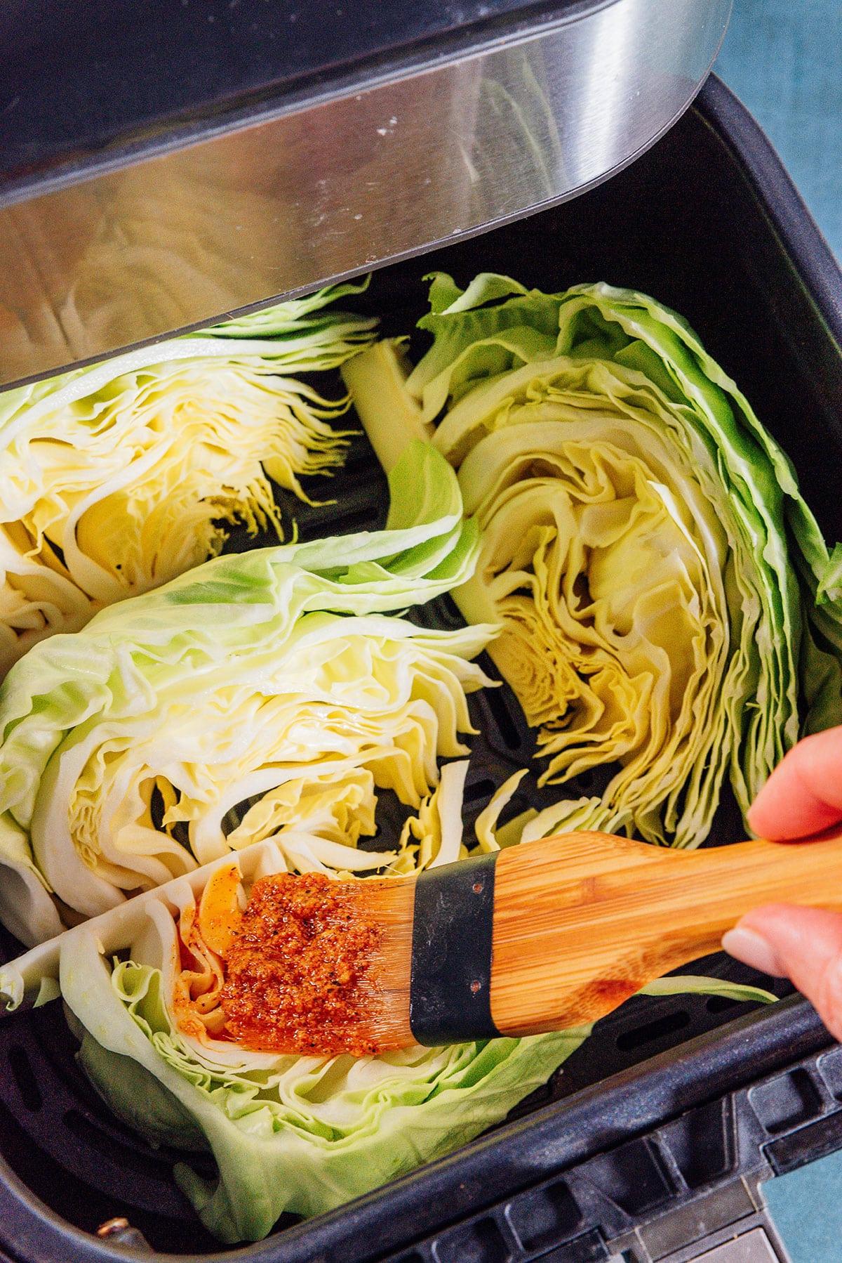 Einfacher Heißluftfritteusen-Kohl 6 Marinade wird mit einem Pinsel auf Kohlspalten in einer Heißluftfritteuse aufgetragen.