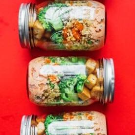 Vegetarisches Stir-Fry Meal Prep Rezeptidee in Einmachgläsern auf rotem Hintergrund