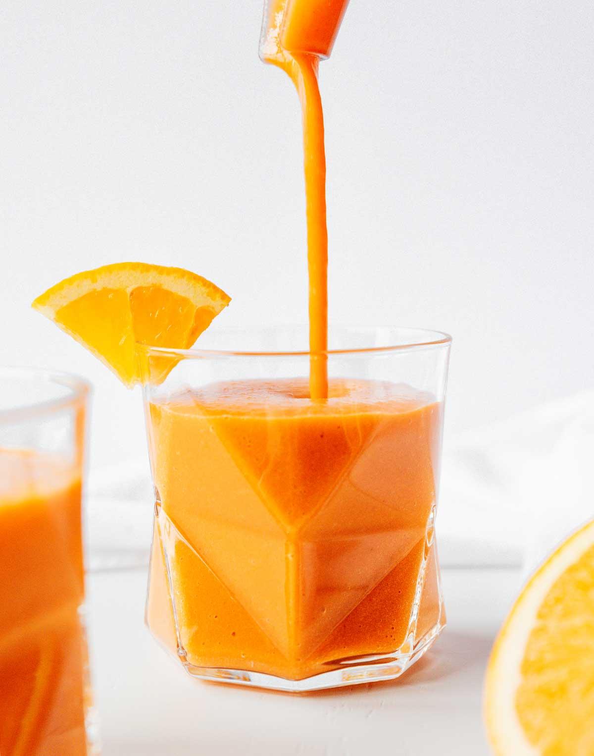 Karotten-Smoothie mit Zitrusfrüchten und Ingwer aus einem Mixer in ein Glas gießen