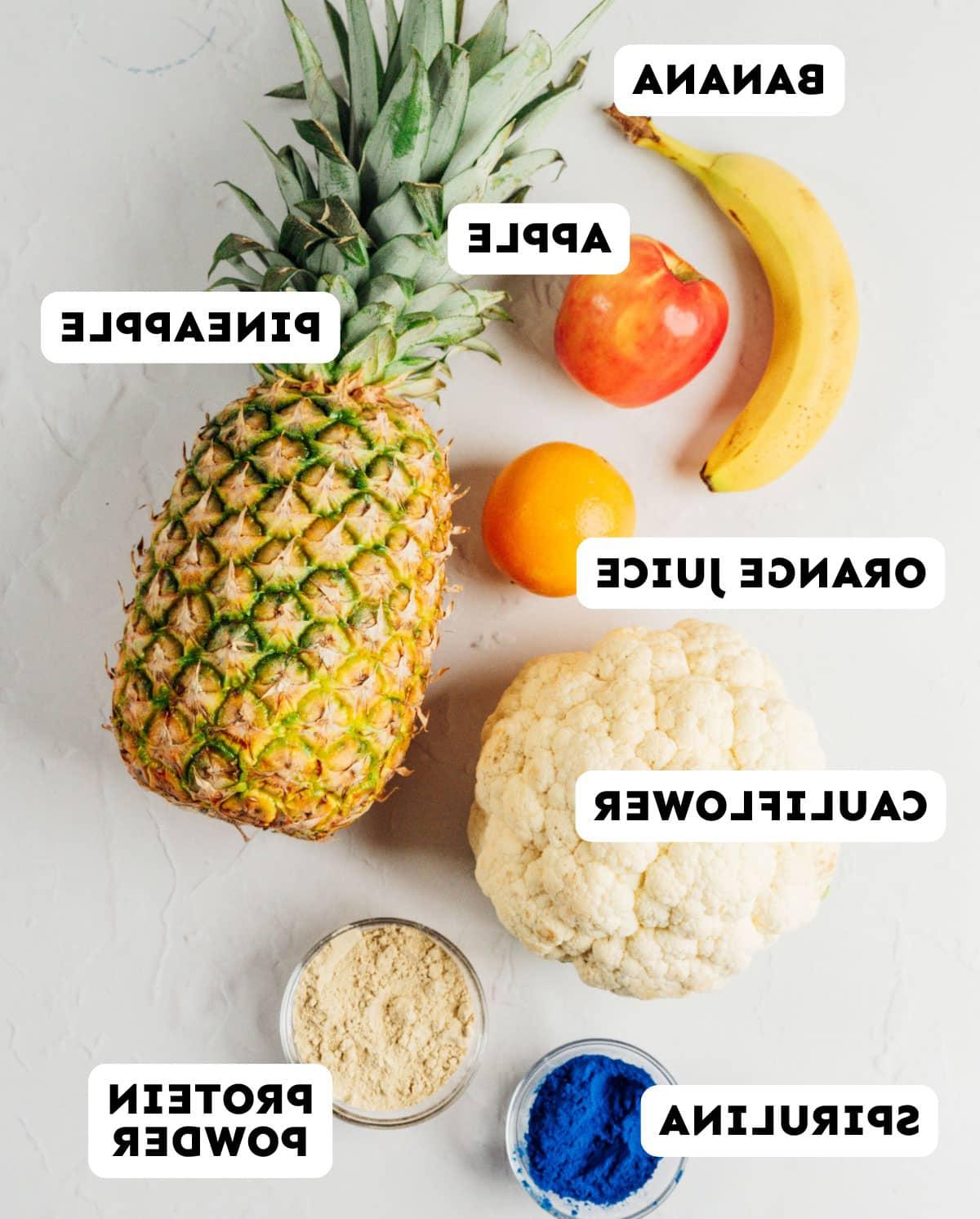 Smoothie-Würfel (Evive-Kopie) 7 Benötigte Zutaten für die Smoothie-Würfel, ordentlich angeordnet: Banane, Apfel, Ananas, Blumenkohl, Proteinpulver, Spirulina, Orangensaft.