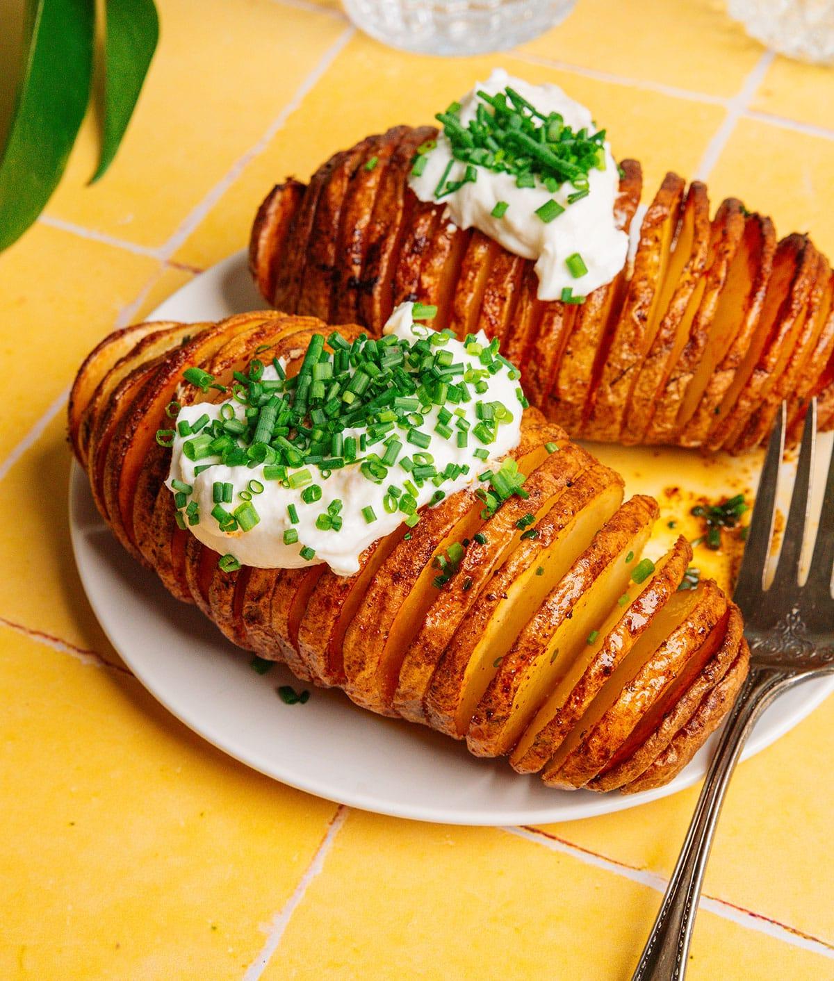 Heißluftfritteusen-Hasselback-Kartoffeln 7 Hasselback-Kartoffeln mit Sauerrahm und Schnittlauch auf einer Platte.