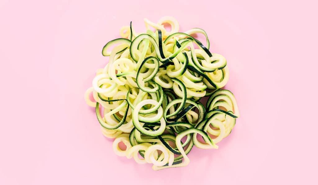 Zucchininudeln zubereiten 7 Ein Stapel Spaghetti-Zucchini-Nudeln auf rosafarbenem Hintergrund.