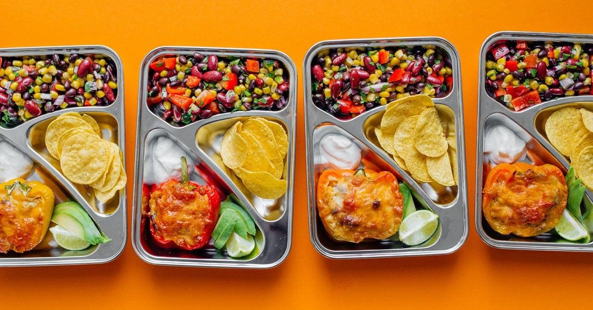 Berühmter Mexikanischer Bohnensalat 7 Meal Prep Behälter mit Bohnensalat und gefüllten Paprika auf orangefarbenem Hintergrund