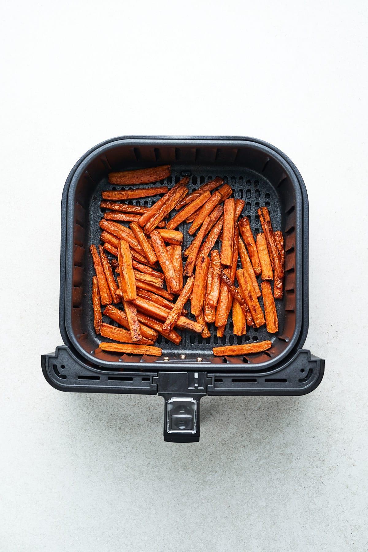Knusprige Karotten-Pommes aus der Heißluftfritteuse 7 Karottenstäbchen im Korb einer Heißluftfritteuse, bereit zum Garen.