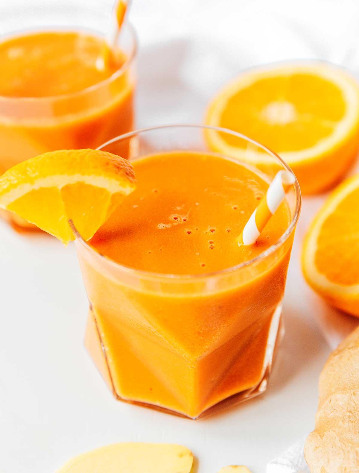 Ein Glas gefüllt mit frisch gemischtem Karotten-Smoothie mit Zitrusfrüchten und Ingwer, garniert mit einer Orangenscheibe