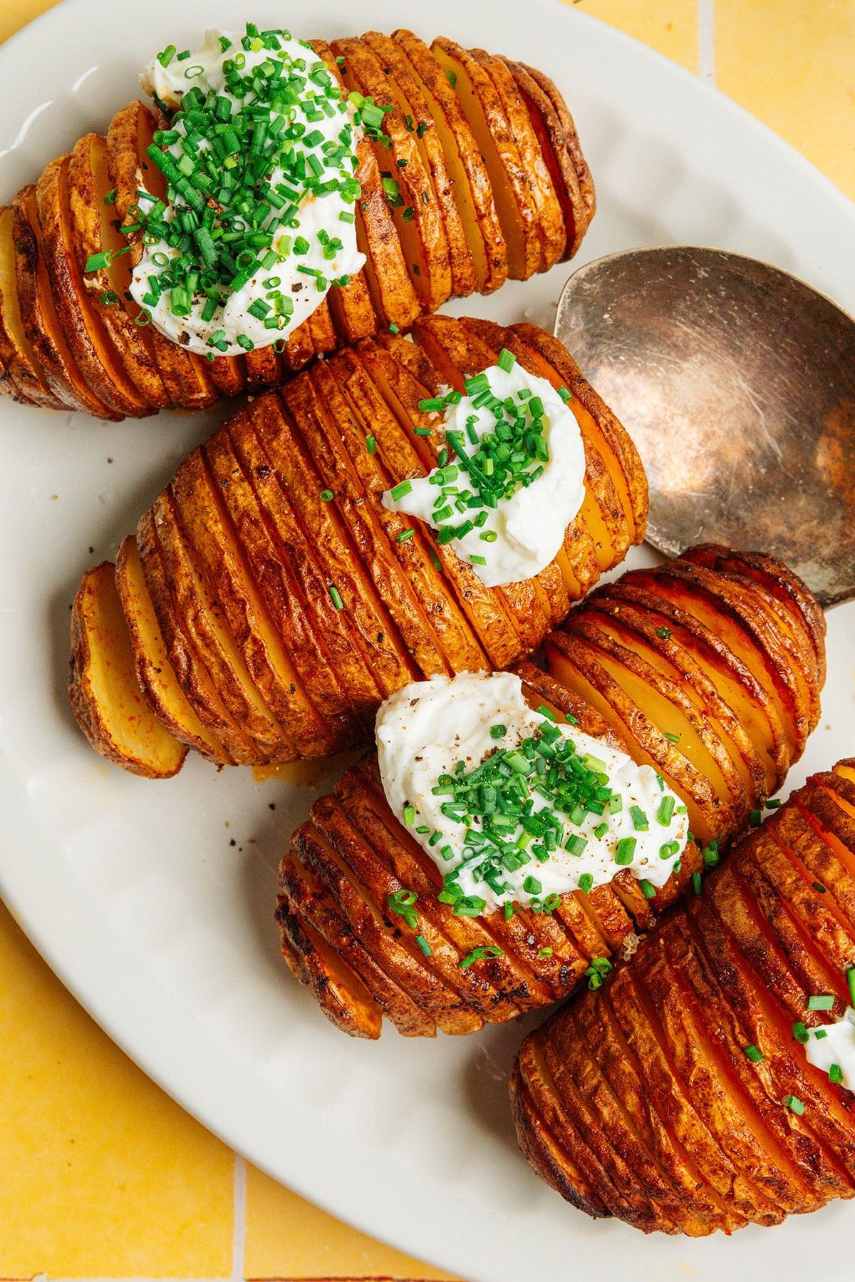 Heißluftfritteusen-Hasselback-Kartoffeln 8 Hasselback-Kartoffeln mit Sauerrahm und Schnittlauch auf einer Platte.