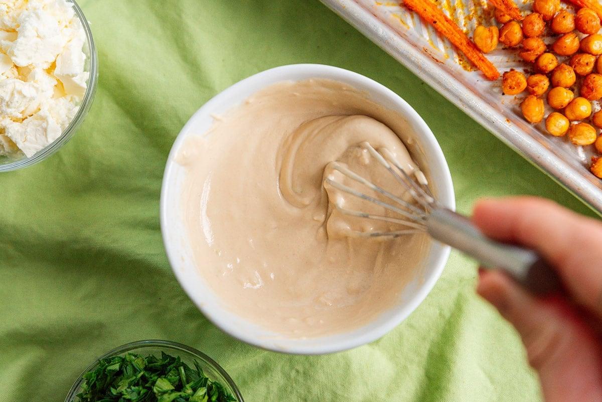 Geröstete Karotten mit knusprigen Kichererbsen 8 Eine Tahini-Sauce wird in einer Schüssel umgerührt, mit glatter, cremiger Konsistenz.