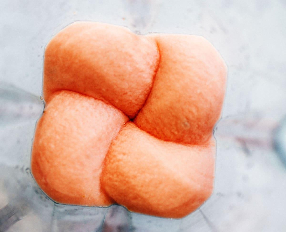 Nahaufnahme von oben eines cremigen orange-rosa Wassermelonen-Daiquiri-Mischung, die in einem Mixer gemixt wird.