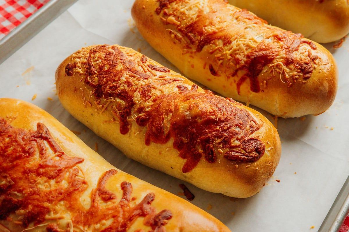 Vegetarischer Costco „Hähnchen“-Auflauf (Mit Kichererbsen!) 8 Nahaufnahme eines Anschnitts eines gefüllten Brotes mit Kichererbsen, geriebenem Käse und Kräutern, auf einem Holzteller. Im Hintergrund sind unscharf eine grüne Pflanze und eine rot-weiß karierte Tischdecke zu sehen. Das Brot hat eine goldbraune Kruste und zeigt eine reiche, dampfende Füllung.