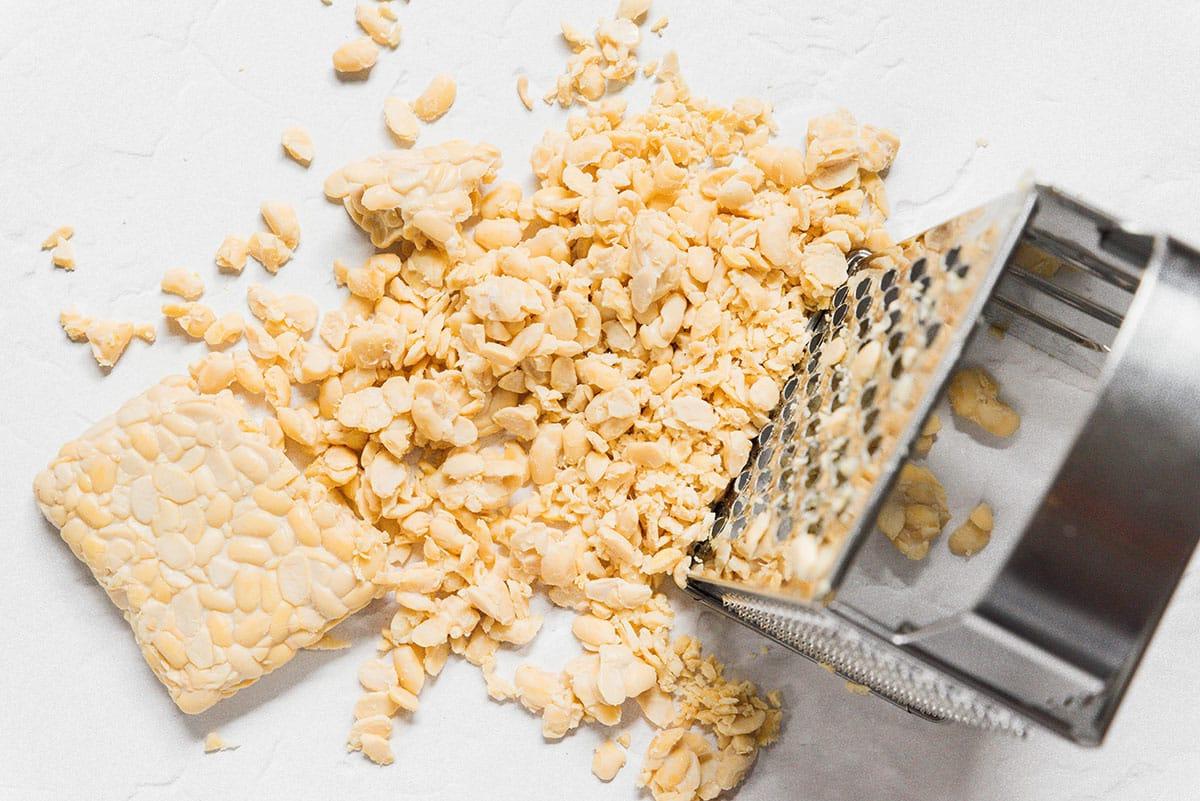 Tempeh wird mit einer Kastenreibe geraspelt.