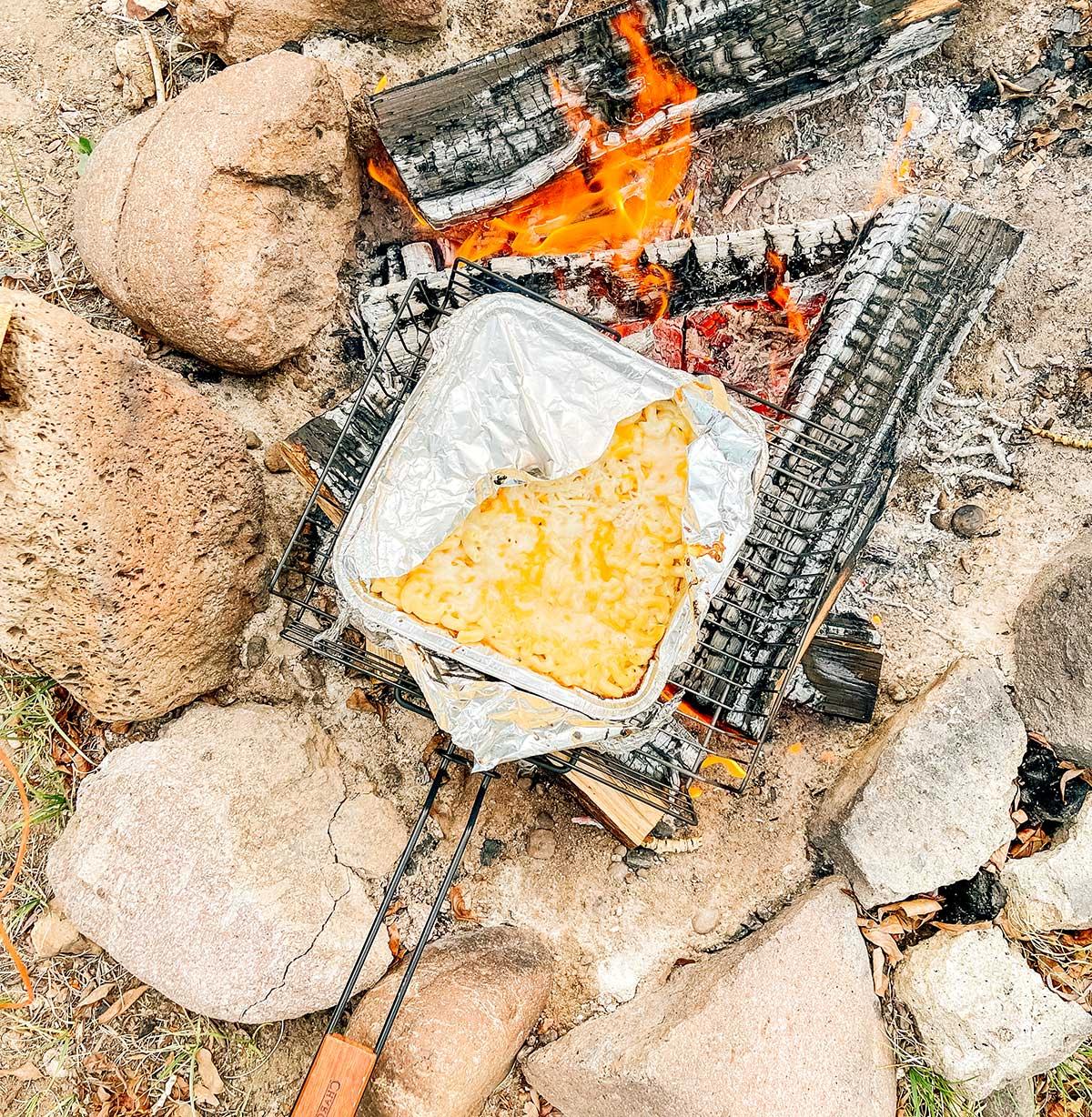 Einfaches Lagerfeuer Mac and Cheese 8 Wegwerf-Aluminiumbehälter mit Lagerfeuer Mac & Cheese wird auf Holzscheiten über einem Lagerfeuer gekocht.