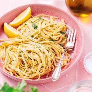 Zitronige Gremolata Pasta (Fertig in 15 Minuten) 8 Ein Teller Gremolata Linguine mit Kräutern und Zitronenspalten, dazu eine Gabel. Im Hintergrund eine Flasche und ein Glas.