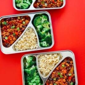Meal Prep Behälter mit Brokkoli, Chili und Bulgur auf rotem Hintergrund - Dieses vegane Tempeh-Chili Meal Prep ist in 30 Minuten fertig und sorgt für das Mittagessen der Woche (außerdem ist es wirklich lecker).