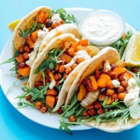 **10 Arten, Hummus zu essen (+ Rezepte!)** 8 Butternut-Wraps auf einem Teller mit blauem Hintergrund – würziger, herzhafter Geschmack, eingewickelt in warme Fladenbrote – das ist das Motto dieser gerösteten Butternut-Kichererbsen-Hummus-Wraps!