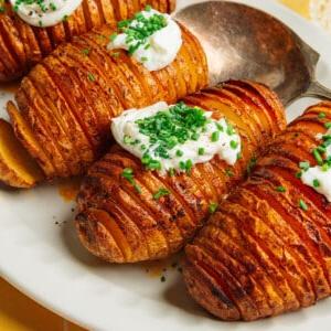 Heißluftfritteusen-Hasselback-Kartoffeln 9 Hasselback-Kartoffeln mit Sauerrahm und Schnittlauch auf einer Platte.