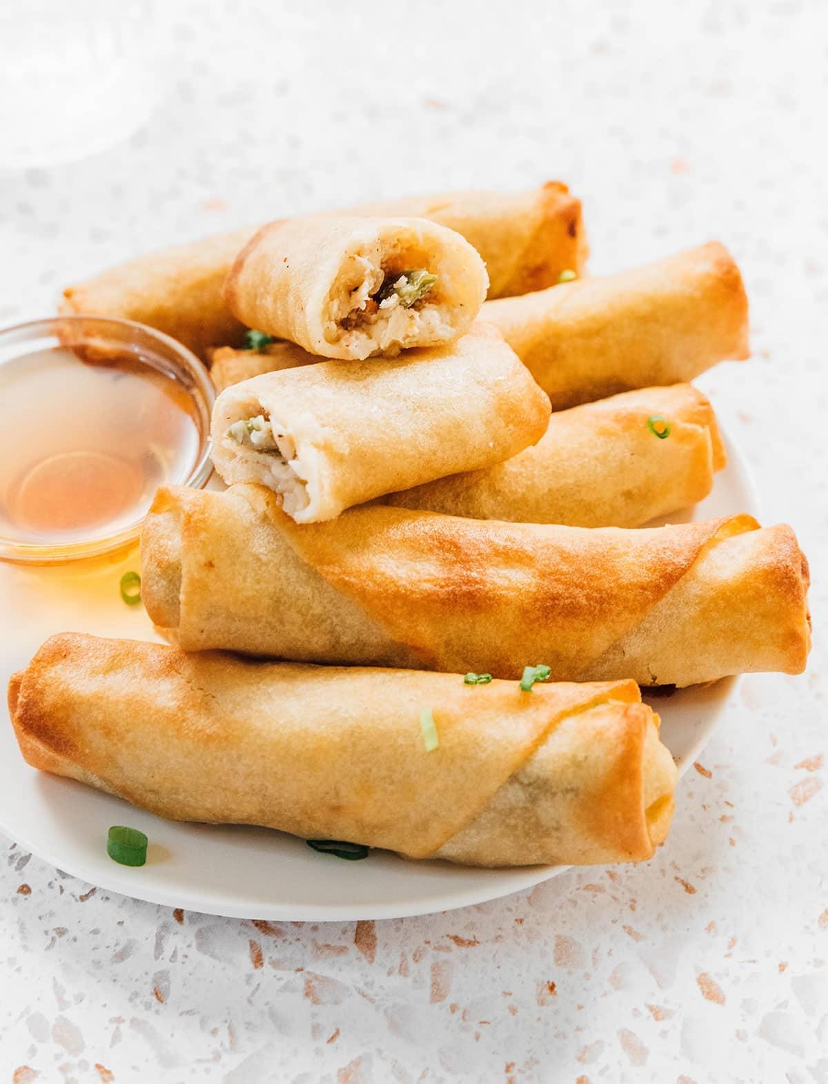Die knusprigsten tiefgekühlten Frühlingsrollen aus der Heißluftfritteuse 10 Heißluftfrittierte tiefgekühlte Frühlingsrollen auf einem Teller, eine davon aufgeschnitten, um die perfekt gegarte Innenseite und goldene Außenseite zu zeigen.