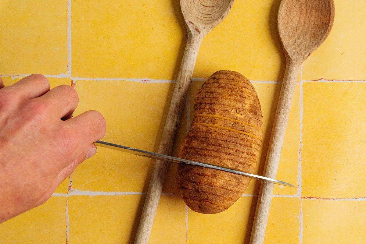 Hasselback-Kartoffeln schneiden mit Löffeln auf beiden Seiten der Kartoffel.