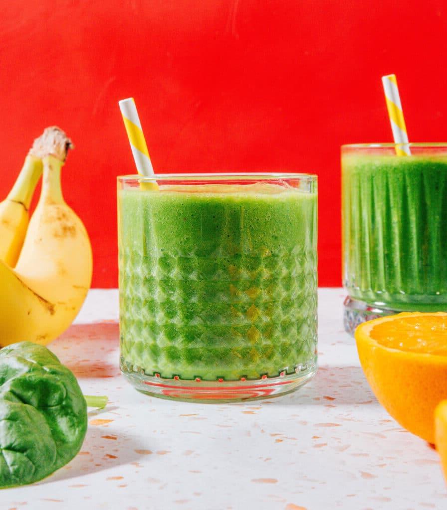 Grünkohl vs. Spinat: Was ist besser? (Mit Fotos!) 10 Grüner Smoothie in einem Glas mit rotem Hintergrund.