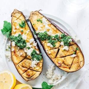 Geröstete Aubergine mit Feta-Minz-Soße 10 Geröstete Auberginen auf einem weißen Teller mit Minze, Feta und Zitrone.