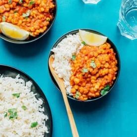 Schüsseln mit Chana Dal und weißem Reis mit Zitronenspalten auf blauem Untergrund, begleitet von erfrischenden Gläsern Wasser.