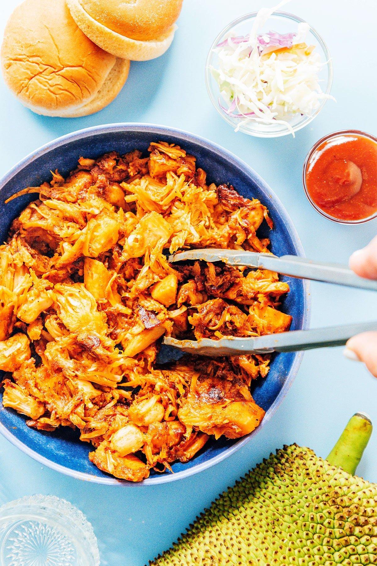 BBQ Jackfrucht Pulled Pork (Fertig in 30 Minuten) 10 BBQ Jackfrucht in einer Schüssel, serviert mit Brötchen, Krautsalat und Barbecue-Sauce.