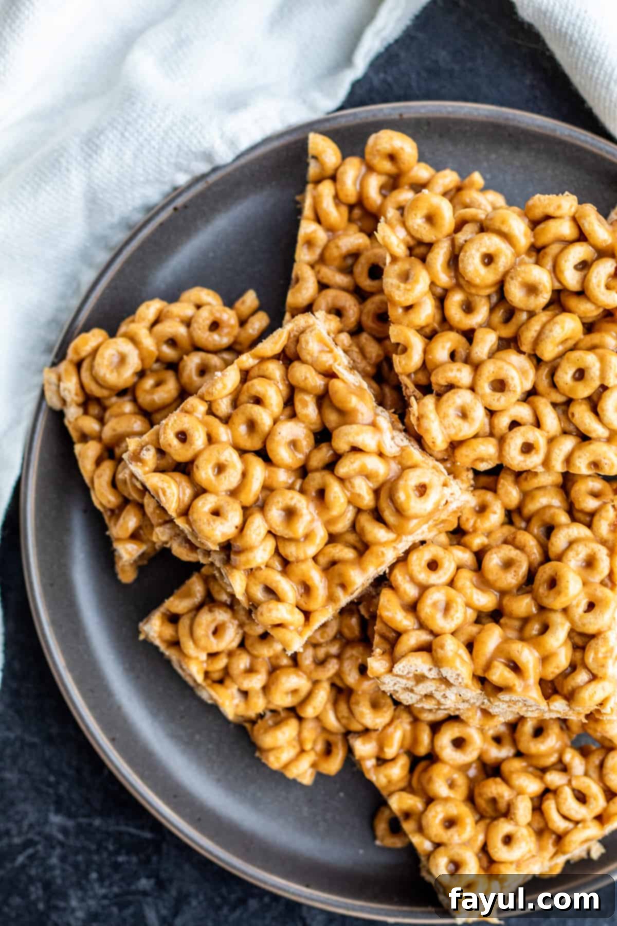 Close-up of golden brown no-bake Peanut Butter Cheerio Bars on a grey plate, ready to be enjoyed.