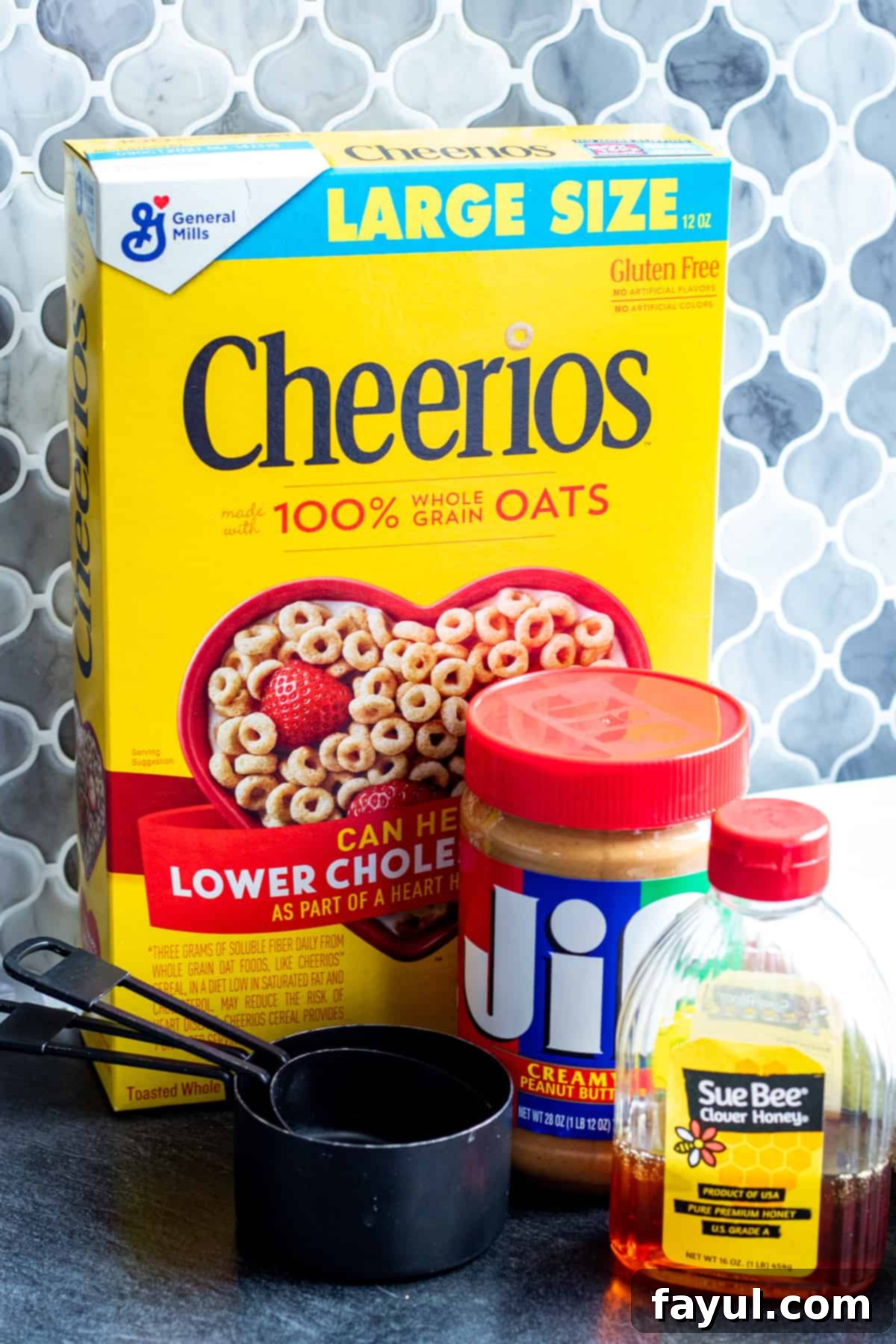 All three simple ingredients for peanut butter cheerio bars laid out on a blue kitchen counter: a bowl of Cheerios, a jar of peanut butter, and a bottle of honey.