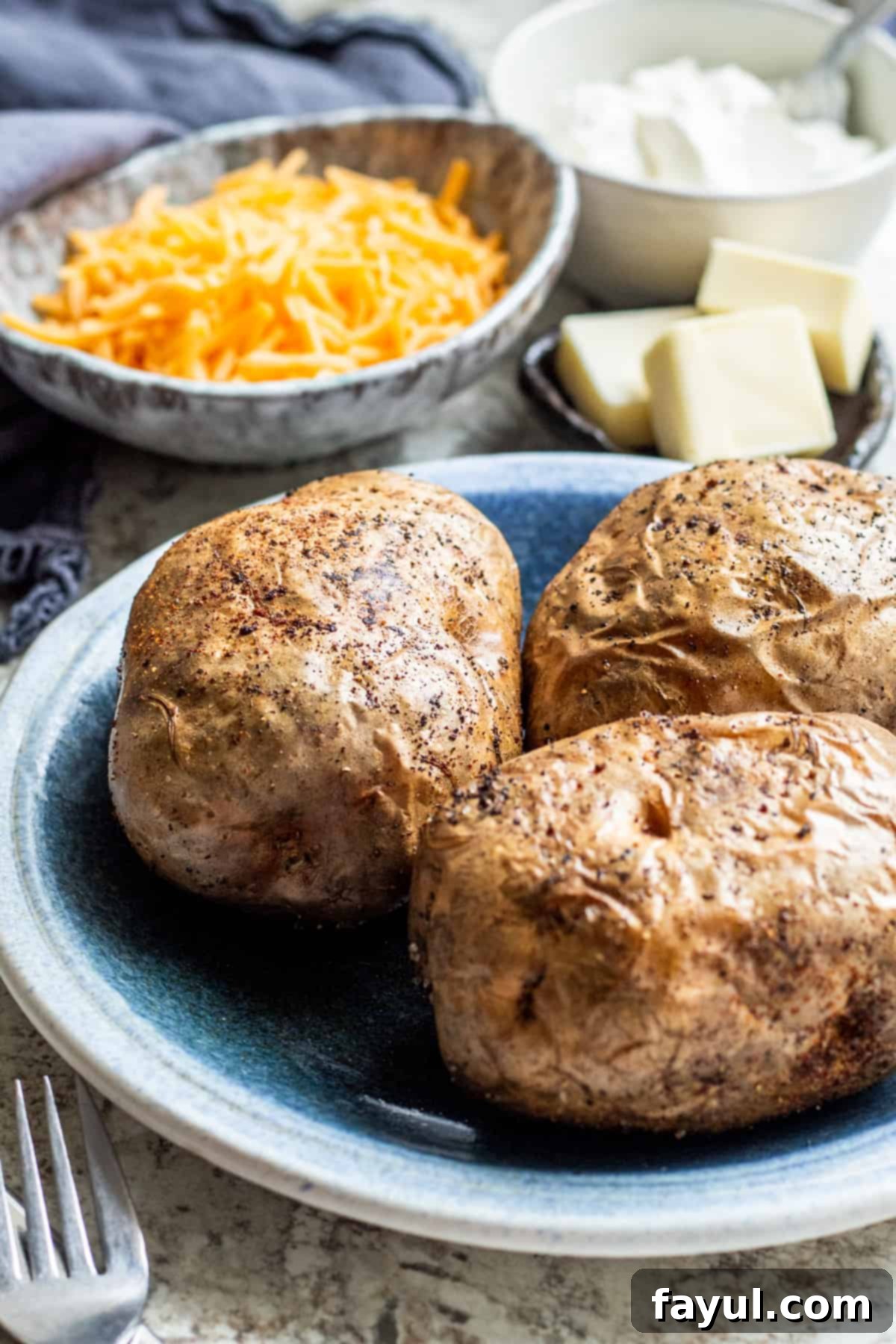 Baked potatoes on a blue plate with toppings in background.