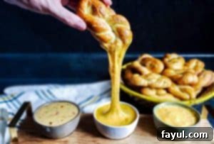 Hand pulling a cheesy homemade soft pretzel from a platter with three cheese dips.