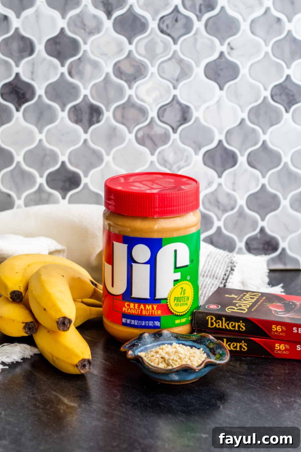 All the essential ingredients for frozen banana bites, including bananas, peanut butter, and chocolate, neatly arranged on a blue counter.