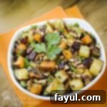 Overhead shot of potato medley garnished with parsley in a white bowl on an orange cloth on a wooden surface.