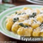 Close up shot fo squash gnocchi sprinkled with shredded parmesan on a green and white striped plate.