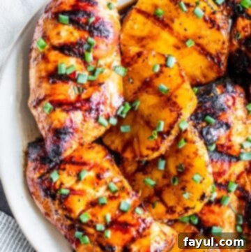 Overhead shot of delicious grilled pineapple chicken with slices of pineapple on a white plate.
