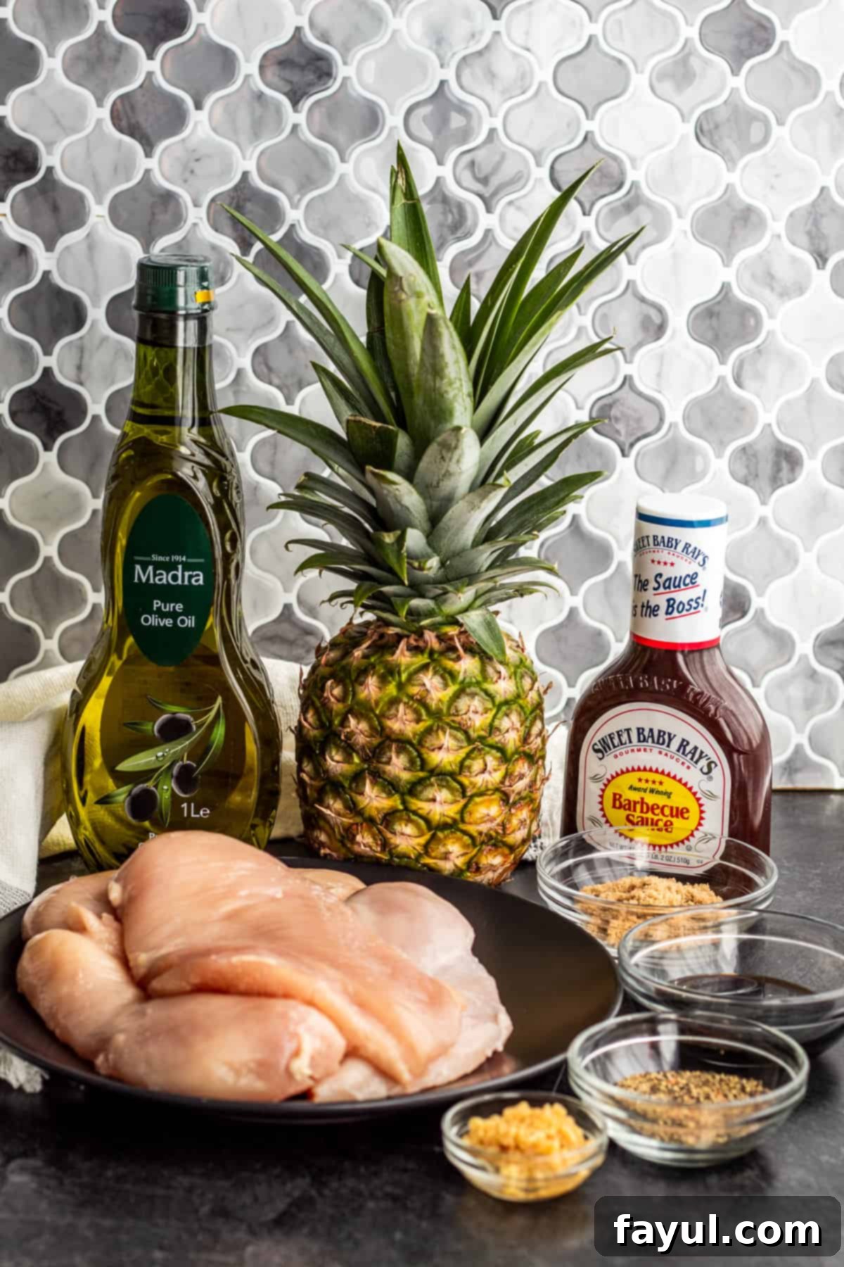 Ingredients for Hawaiian BBQ chicken laid out on a gray counter, including pineapple, chicken, and sauces.