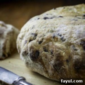 Side view of whole loaf of olive bread on a wooden cutting board with a butter knife on the side.