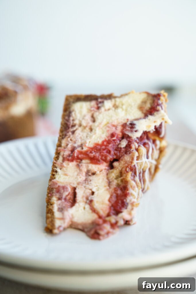 A beautifully presented whole Roasted Strawberry Crumble Cheesecake with a perfect slice removed, showing off its creamy layers and rich filling.