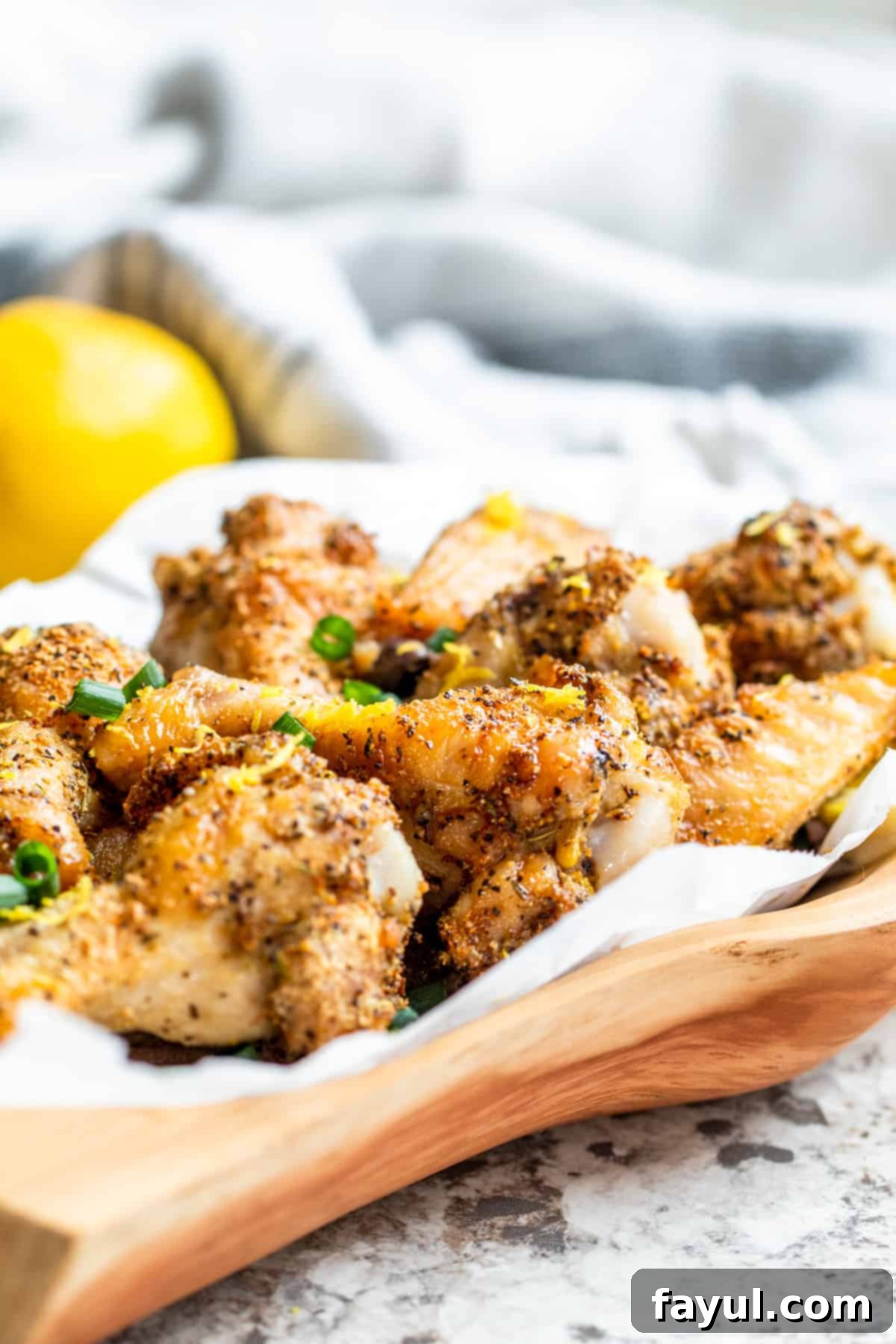Crispy Air Fryer Lemon Pepper Chicken Wings 2 Wooden bowl filled with lemon pepper wings on white counter.