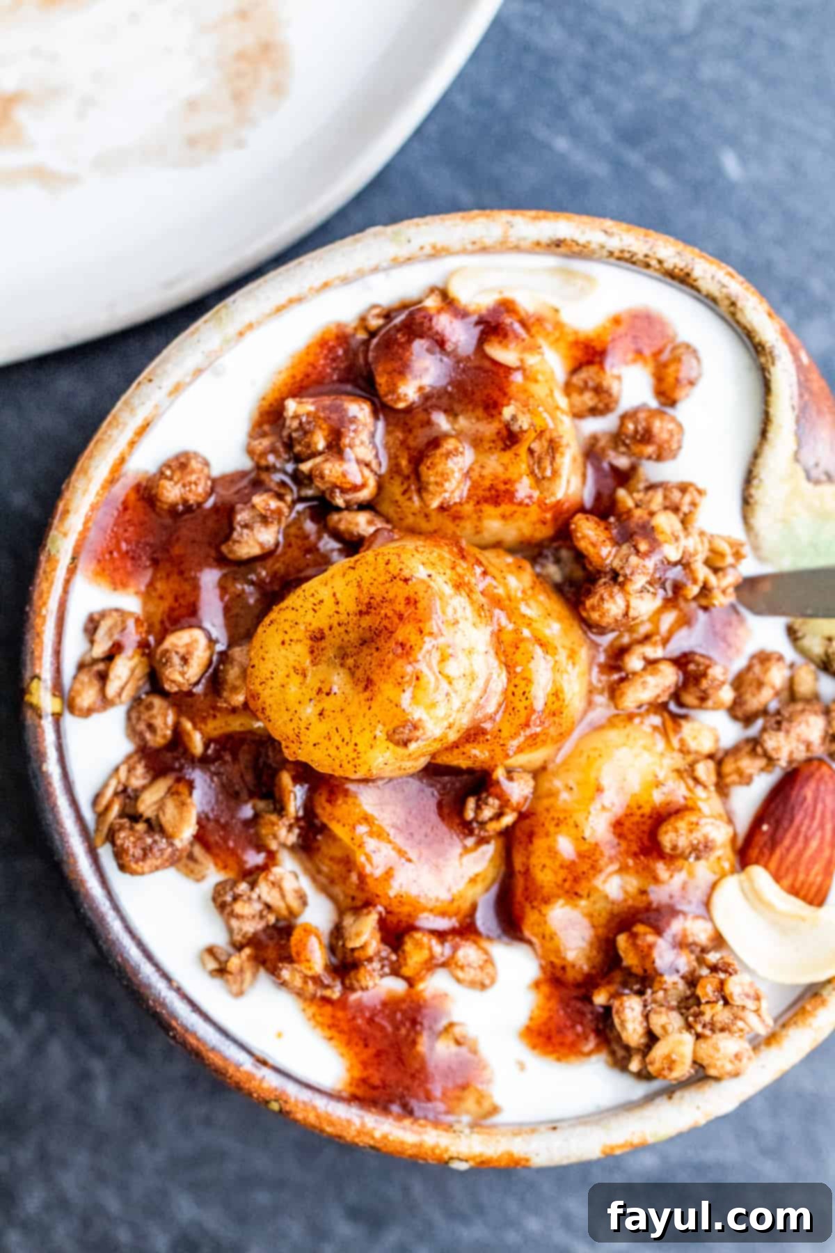 Overhead shot of bananas on top of granola and yogurt in small tan bowl.