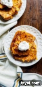 Shot from above photo for crispy french toast recipe. There are two white plates with two pieces of french toast on each. Each plate also have whipped cream on it and are slightly out of frame. The plates are sitting on a dark wooden surface and at the bottom of the shot is a white towel with blue and yellow plaid design. 